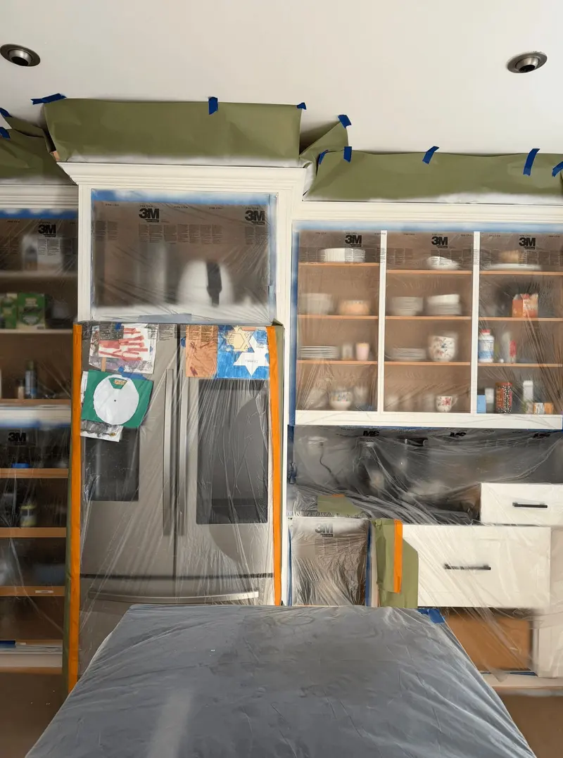 Cabinets and refrigerator masked with tape and plastic during spraying