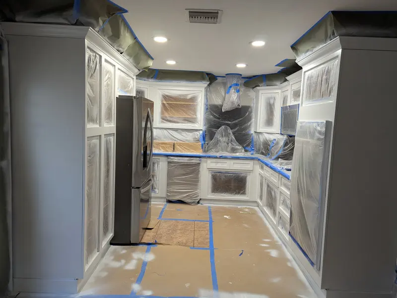 A kitchen fully sealed with plastic and tape during cabinet priming